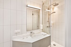 A modern bathroom with a large mirror, a sink, and a shower. - H+ Hotel Wien (Vienna)