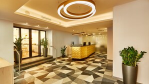 Un hall d’hôtel moderne avec un sol à motifs géométriques, un comptoir d’accueil et des plantes en pot.