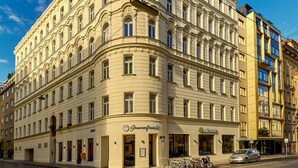 Un immeuble d’angle au style architectural classique, doté de nombreuses fenêtres et d’une entrée au niveau du rez-de-chaussée.