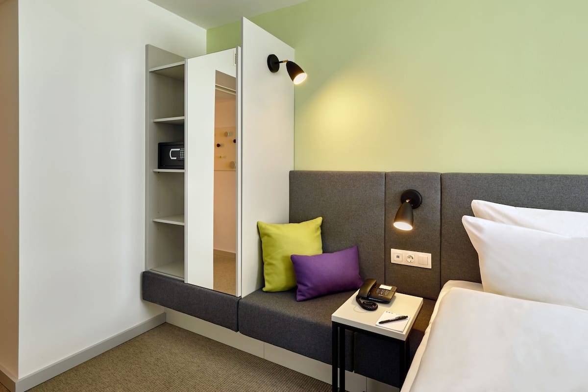 Ein Hotelzimmer mit Bett, Nachttisch, Lampe und einem eingebauten Kleiderschrank mit Regalen.