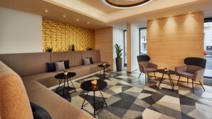 Un hall d’entrée moderne avec un sol à motifs géométriques, un canapé d’angle, une table ronde et deux fauteuils.