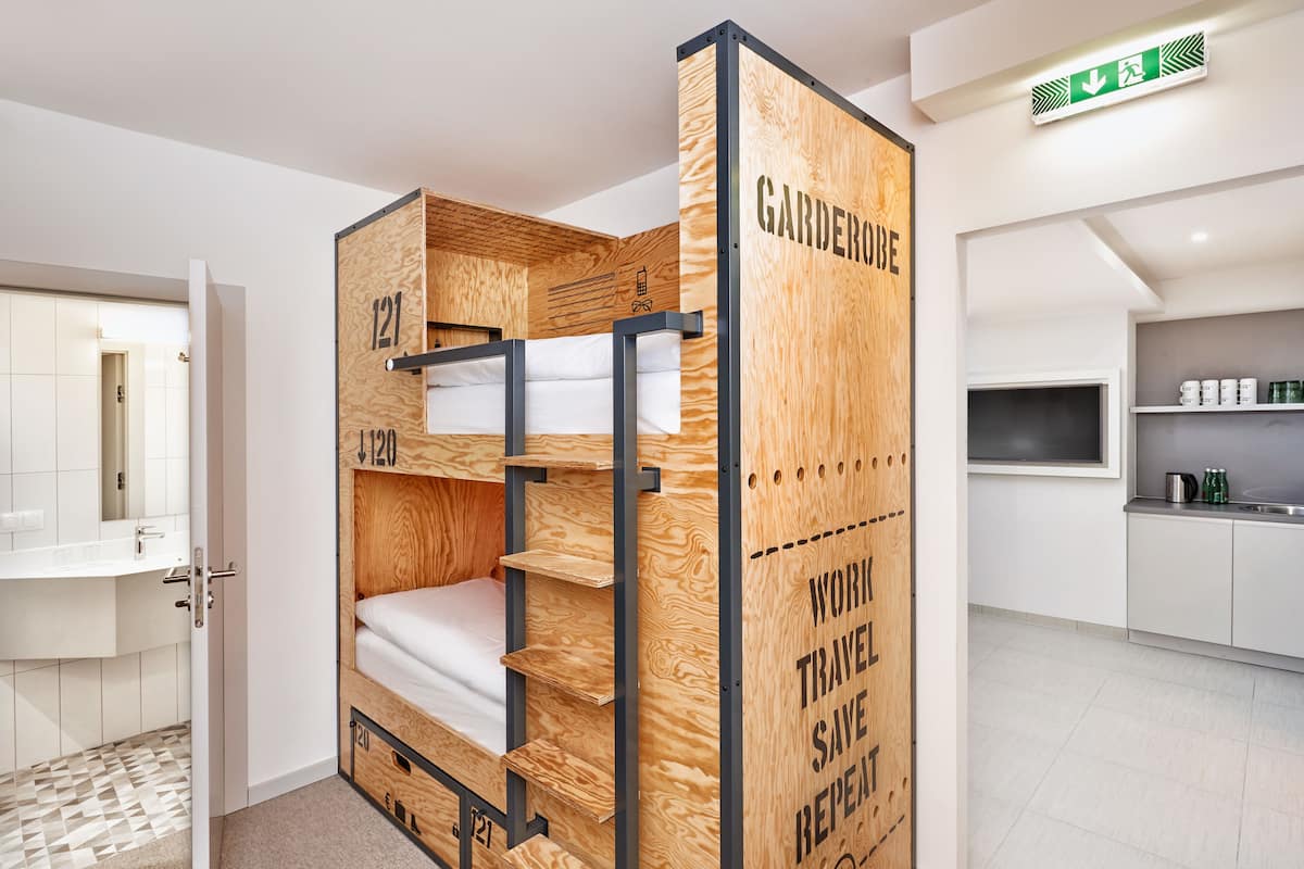 Ein Stockbett mit Holzaußenverkleidung und Metallrahmen, beschriftet mit Zimmernummern und einer Botschaft zum Thema Nachhaltigkeit.