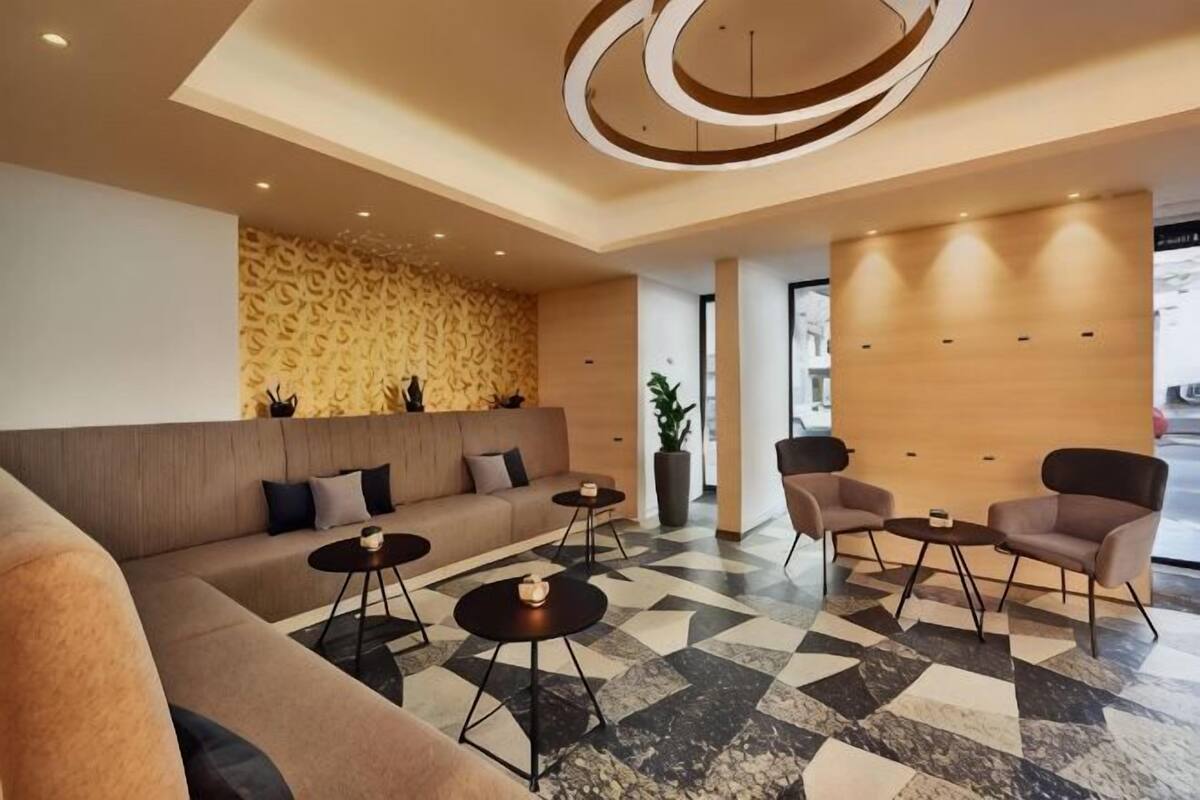 Eine moderne Lobby mit einer Couch, Sesseln, einem Couchtisch, einem gemusterten Boden und einer dekorativen Deckenleuchte.