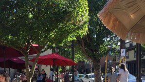Een terras met stenen muren en houten tafels, omringd door bomen en parasols.