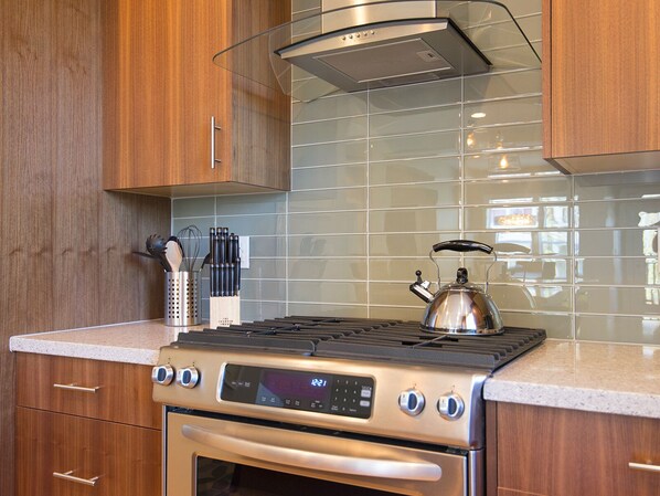 A kitchen with a stainless steel stove, oven, and a kettle on the counter.