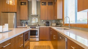 Een moderne keuken met houten kastjes, roestvrijstalen apparatuur, een gasfornuis en een groot raam dat voor natuurlijk licht zorgt.