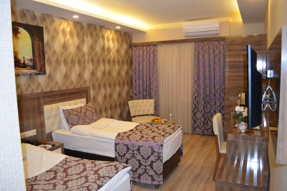 A hotel room with a bed, two chairs, a small table with a vase, and a painting on the wall.