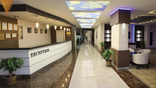Zona de recepción de hotel con mostrador, certificados enmarcados en la pared y un techo con diseño de nubes.