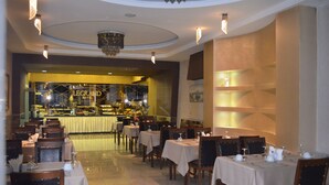 Un restaurante con mesas dispuestas para comer, una zona de bar al fondo y un candelabro en el techo.