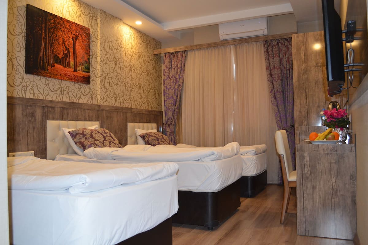 A hotel room with two beds, a wooden headboard, a painting, an air conditioning unit, and a small table with fruit.