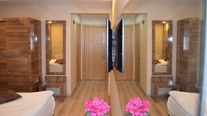 Una habitación de hotel con piso de madera, un espejo grande, un televisor de pantalla plana y dos camas.