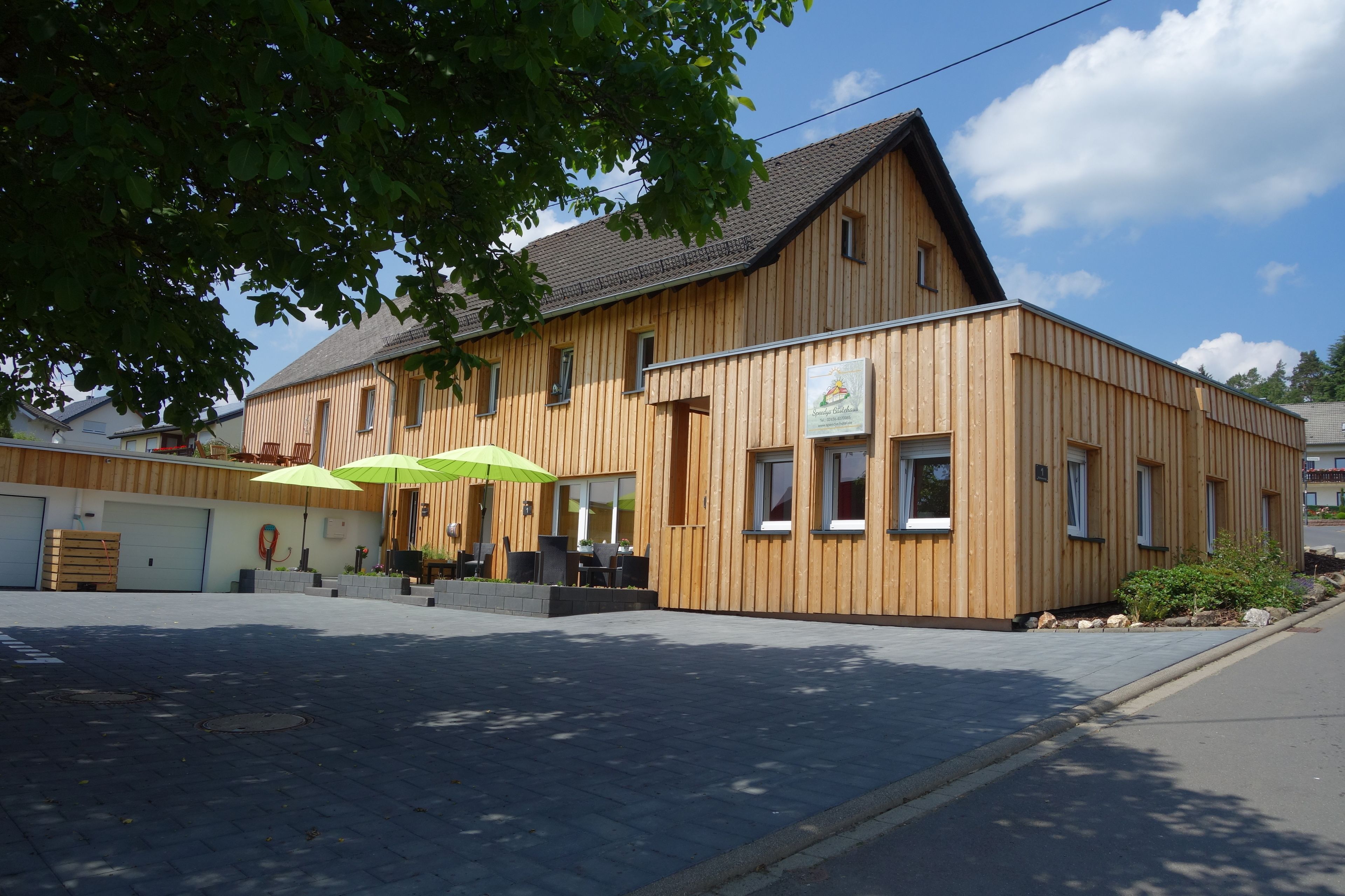 A wooden building with a sloped roof, a visible sign, and outdoor seating with umbrellas.