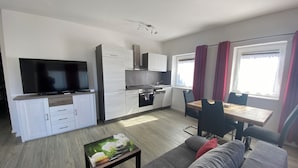 Une cuisine moderne avec des meubles blancs, un four encastré et un coin repas comprenant une table et des chaises.