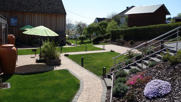 Une cour avec un chemin pavé, des plantes vertes et un bâtiment en bois.