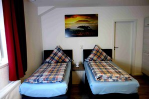 A room with two single beds, a painting of a sunset, a white door, and a radiator. - Race & Rest Apartments (Baar)