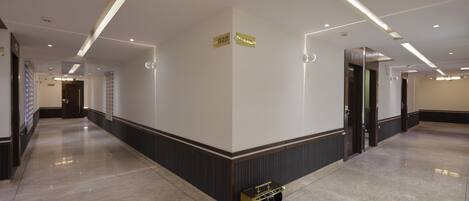 A spacious hotel corridor with a polished marble floor, modern lighting fixtures, and directional signs.