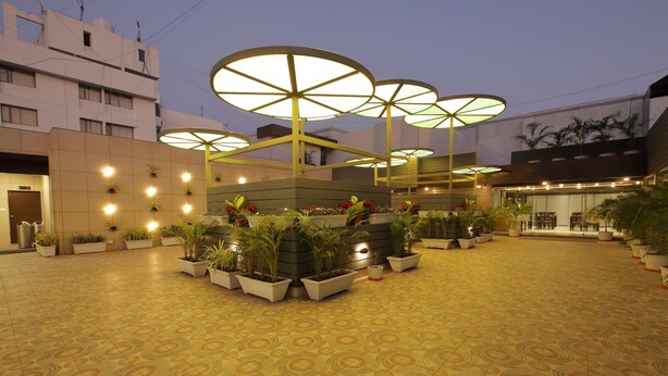Un patio amplio con pavimento decorativo, plantas en macetas y grandes sombrillas que dan sombra.