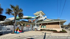 A theme park entrance with a water slide, a building with a sign, and a 'No Parking' sign on the street. -  Ocean Lakes. Pet friendly One Story  with ramp. Complimentary golf cart. (Myrtle Beach)