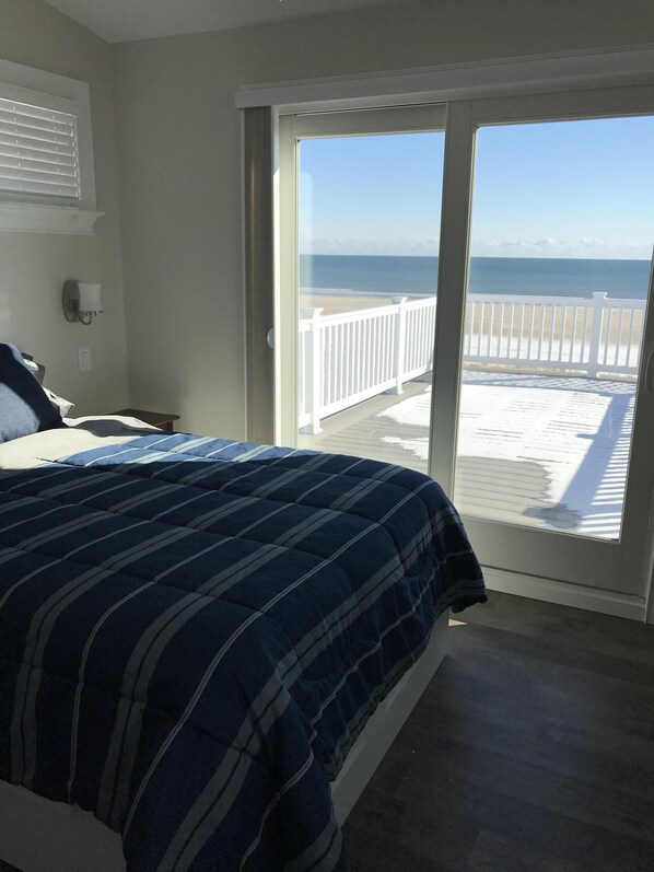 A bedroom with a bed, a nightstand, a phone, and a view of the beach through a sliding glass door. - Ocean Front, Single Family Home with 5 BR, 4.5 Baths and 4 large decks (Ocean City)