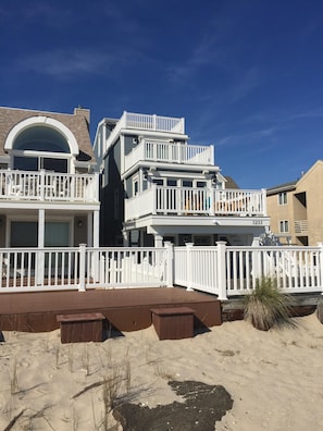 A multi-story house with a white exterior, a balcony, and a sandy front yard. - Ocean Front, Single Family Home with 5 BR, 4.5 Baths and 4 large decks (Ocean City)