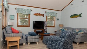 Ein gemütliches Wohnzimmer mit Fernseher, zwei Sofas, einem Couchtisch und Fisch-Wandbildern.