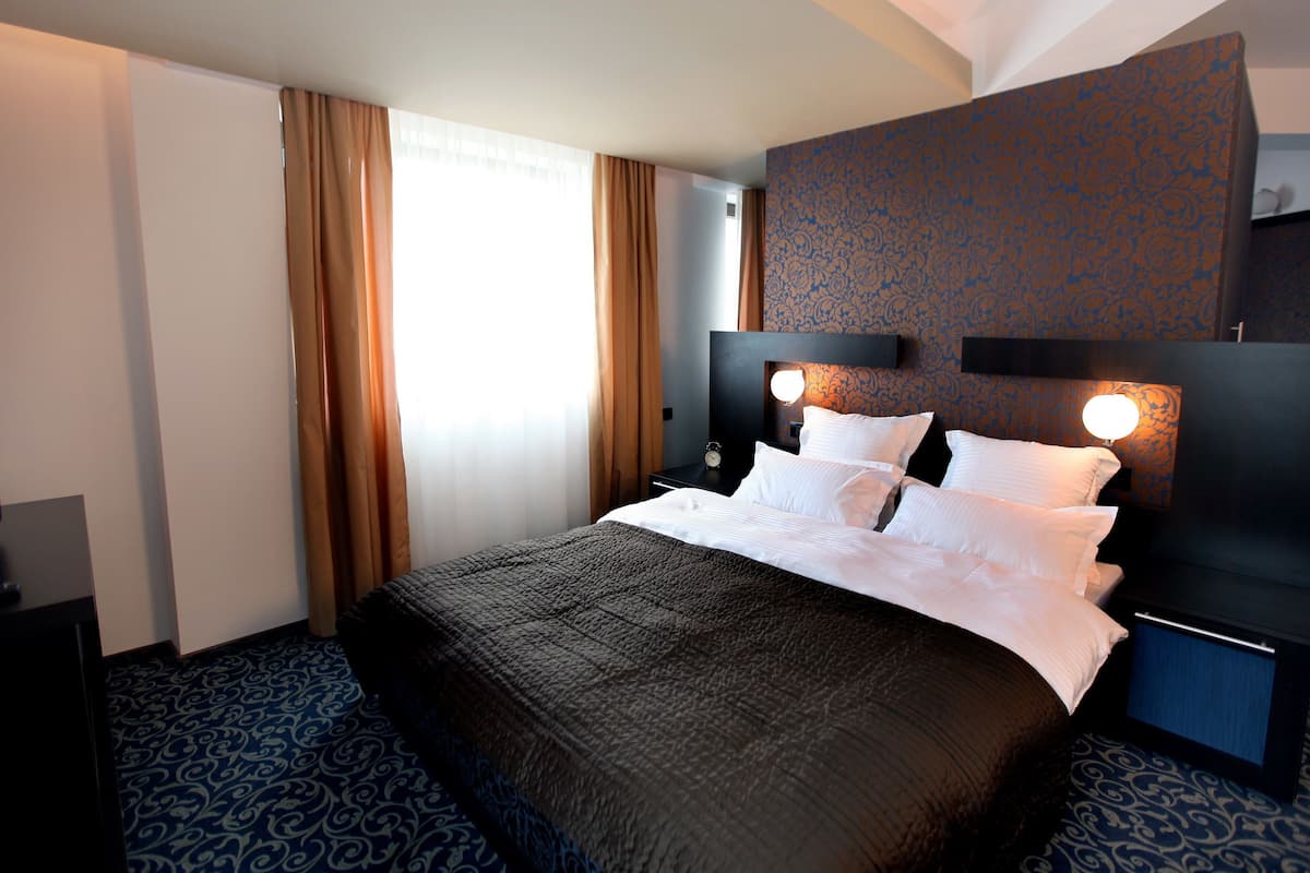 A hotel room with a large bed, a nightstand, a wall-mounted lamp, and a patterned carpet.