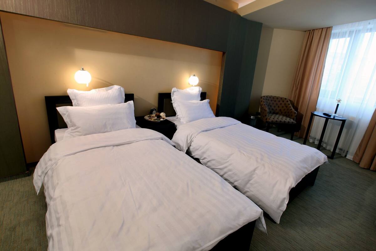 A hotel room with two beds, a nightstand, a chair, and a small table.