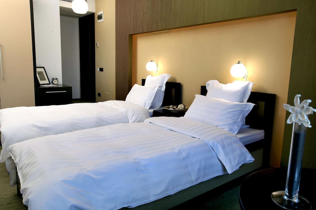 A hotel room with two beds, bedside tables, a nightstand, a mirror, and a decorative flower vase.