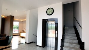 A modern lobby with a reception desk, a clock, an elevator, and a staircase.