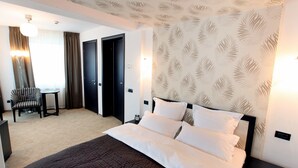 A hotel room with a large bed, a chair, a small table, and a desk.