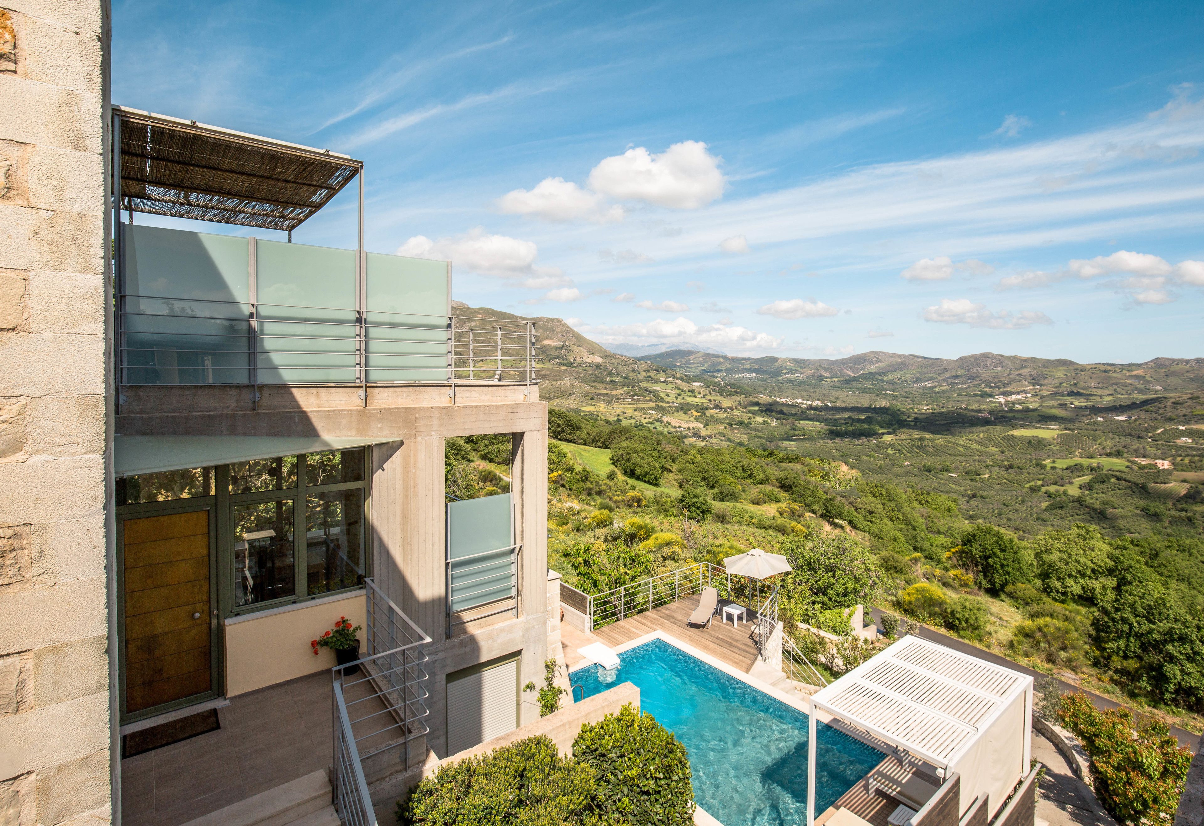 A modern house with a swimming pool, a balcony, and a view of the countryside.