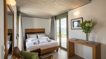 A hotel room with a large bed, a wooden nightstand, a chair, a desk, a vase with flowers, and a view of the outdoors.