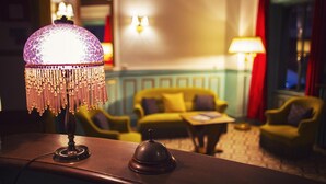 Ein schwach beleuchteter Raum mit einer Tischlampe, einer Holztresore und einem gelben Sofa im Hintergrund.