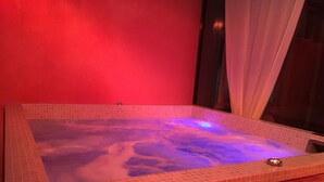 Ein Whirlpool mit gefliestem Innenraum und Holzunterbau vor einer roten Wand.