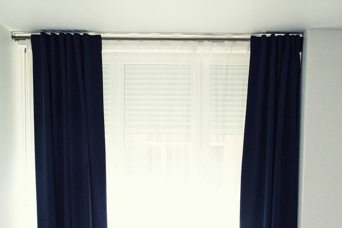 A hotel room with two single beds, a small table, and a window with curtains.