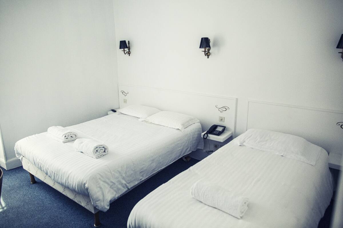 A hotel room with two single beds, each with white linens and a small bedside table with a telephone.