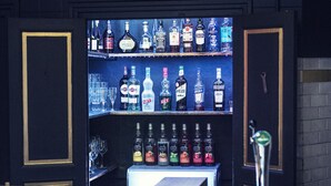 Eine Bar mit einer Pendelleuchte, Regalen voller Spirituosenflaschen und Hockstühlen.