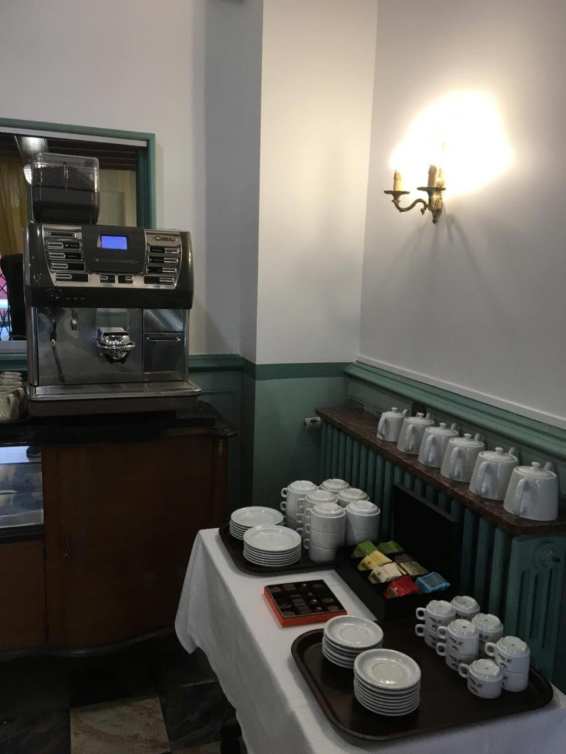 A buffet setup with a coffee machine, plates, mugs, and condiments.
