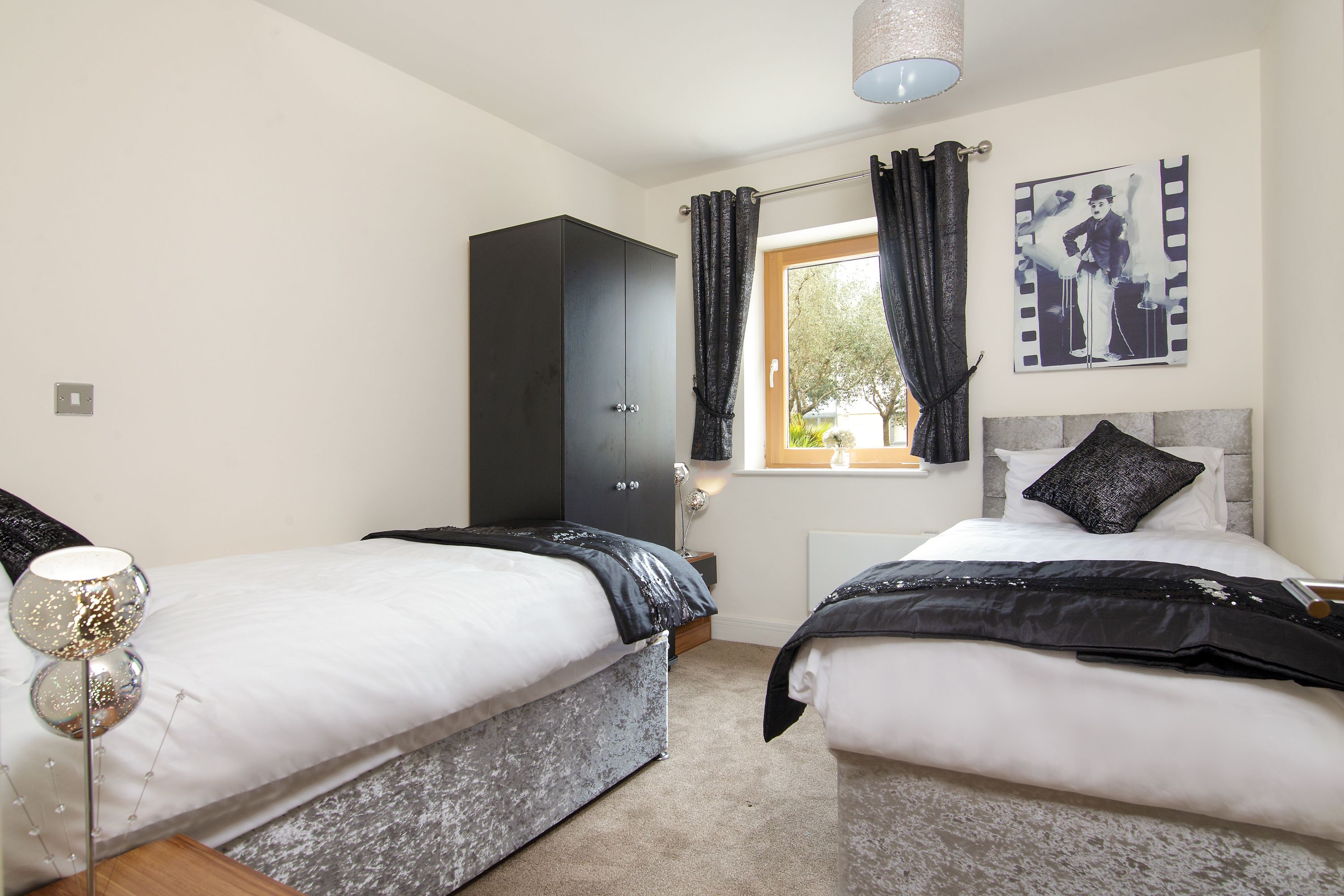 A bedroom with two beds, a wardrobe, a lamp, and a window with curtains.