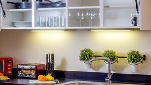 Una cucina con mobili bianchi, un tostapane rosso, un lavandino e due piante in vaso appese alla parete.