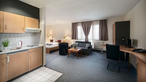 A compact hotel room with a kitchenette, a sofa, a dining table, and a TV. - Sunibel Inn Hotel (Reinheim)