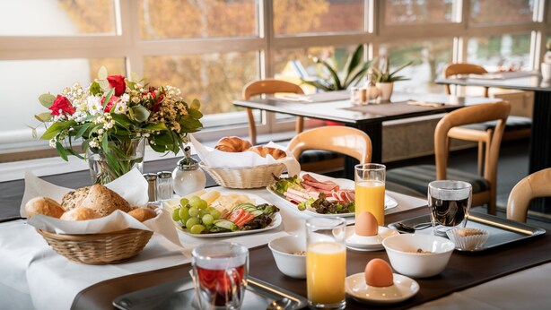 A breakfast setting with a table set for two, including croissants, a fruit platter, eggs, and juice. - Sunibel Inn Hotel (Reinheim)