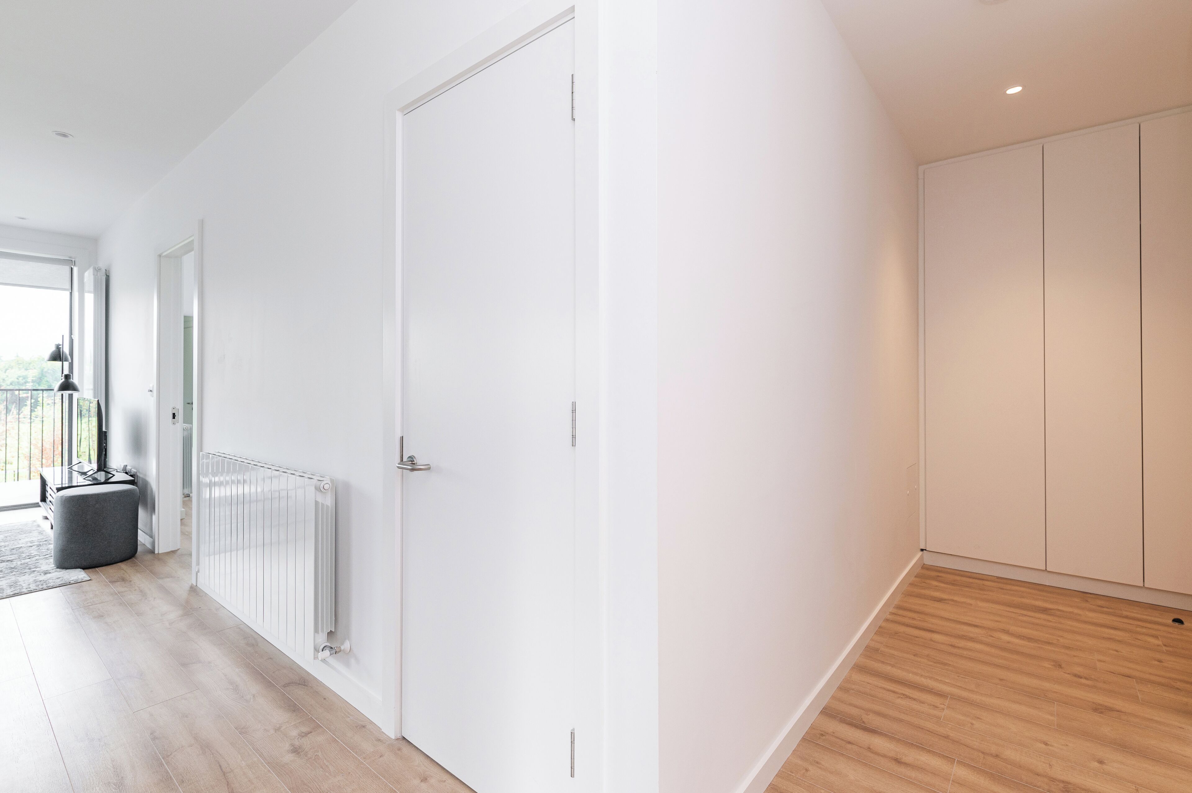 A modern, minimalist room with a white door, a radiator, and a wooden floor.