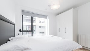 A modern bedroom with a large bed, a window with a view of buildings, and a wardrobe. - The Grange Dublin (Dublin)
