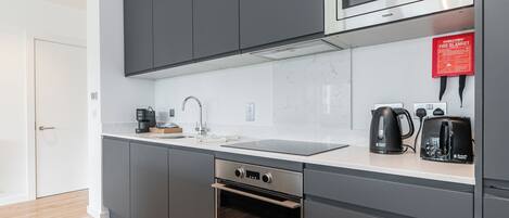 Una cocina moderna con gabinetes grises, un microondas de acero inoxidable, un horno empotrado, una cafetera y un tostador.