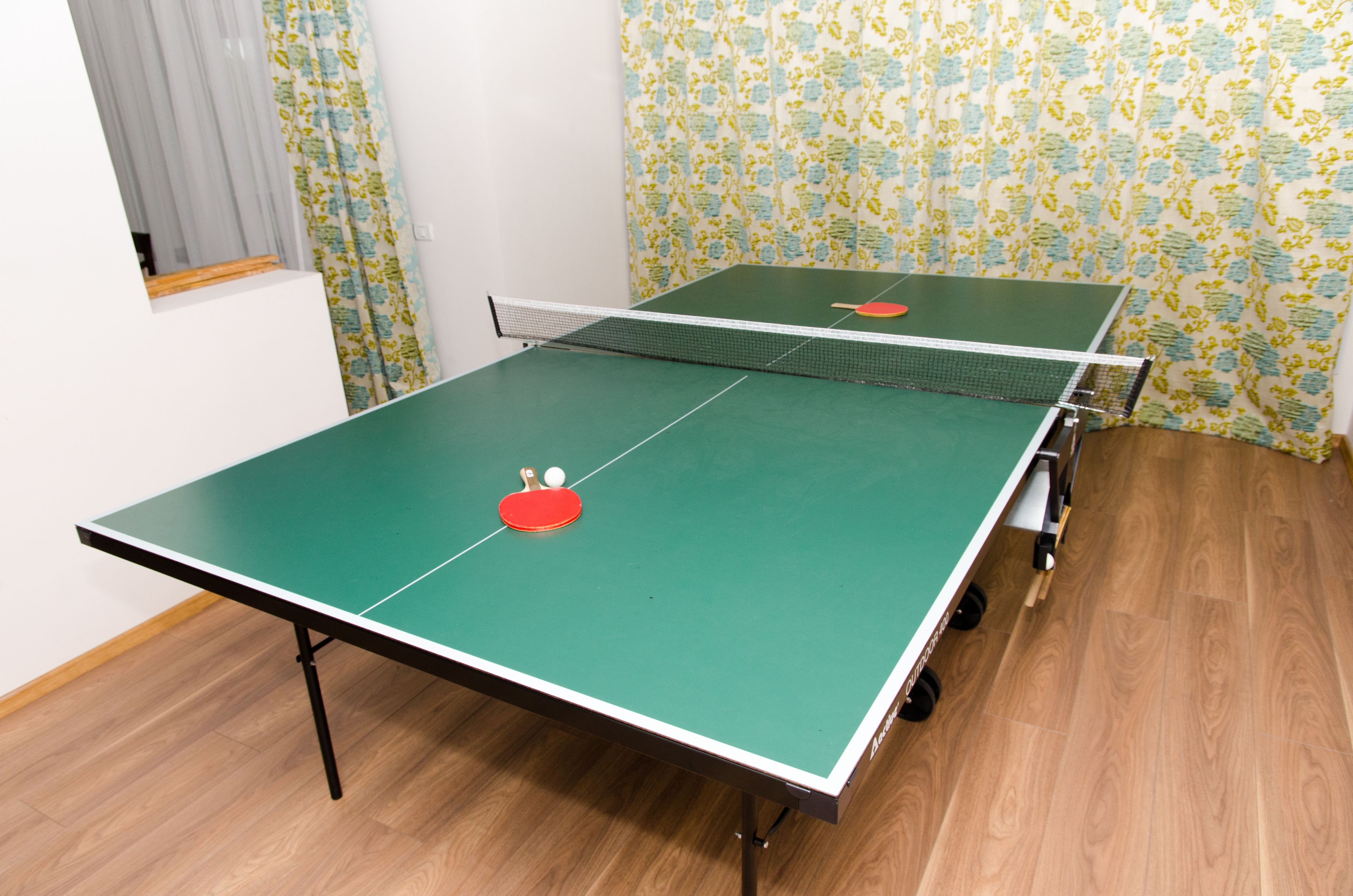 A ping pong table with a net in a room with floral wallpaper and wooden flooring.