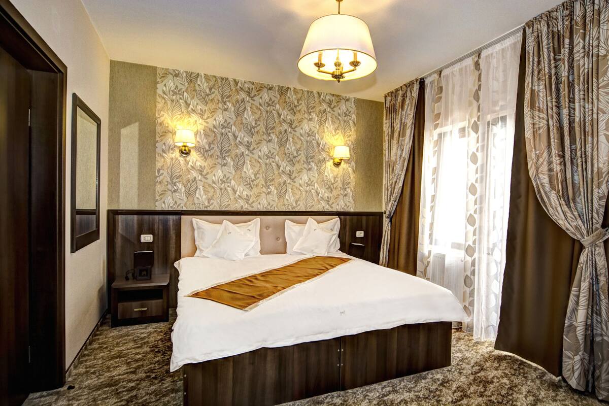 Een hotelkamer met een groot bed, twee wandlampen, een hoofdeinde, een nachtkastje en een vloerbedekking.