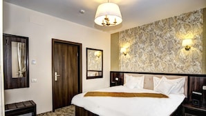 Habitación de hotel con una cama grande, cabecera de madera, dos lámparas de noche, un banco, un espejo y un papel tapiz estampado.