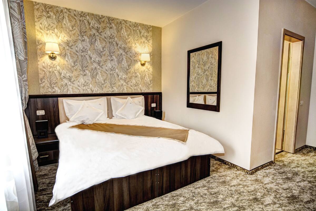 Een hotelkamer met een groot bed, twee wandlampen, een spiegel en een vloerbedekking.