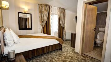 A bedroom with a bed, a bedside table, a mirror, and a bathroom visible through an open door.